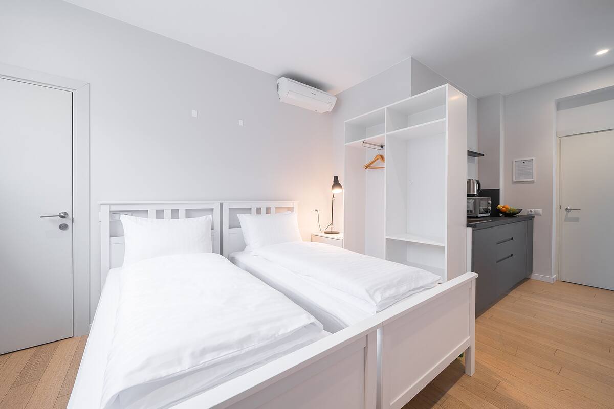 A modern bedroom with a white bed, a bedside table with a lamp, and a built-in wardrobe.