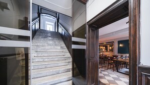 A staircase with a black railing leading to a dining area with a checkered floor and wooden furniture. - Lollo Self Check-in Residence - Lollo Luxury (Vilnius)
