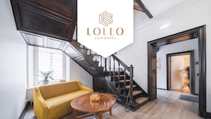 A spacious living area with a yellow sofa, a round wooden coffee table, and a dark wooden staircase. - Lollo Self Check-in Residence - Lollo Luxury (Vilnius)