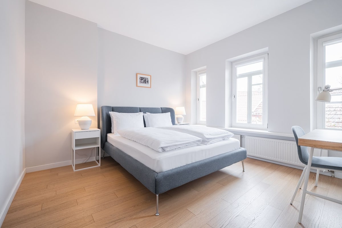 A modern bedroom with a bed, bedside tables, a desk, and a chair.