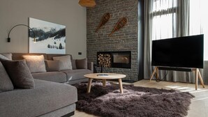 A modern living room with a grey sofa, a round wooden coffee table, a fireplace with logs, and a flat-screen TV on a stand. - VIP RESIDENCES ANDORRA (El Tarter)