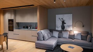 A modern kitchen with grey cabinets, a built-in oven, and a dining area with a grey sofa and a small round table. - VIP RESIDENCES ANDORRA (El Tarter)