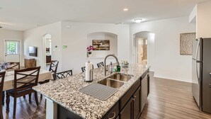 A modern kitchen with granite countertops, stainless steel appliances, and a dining area with wooden chairs and a table.