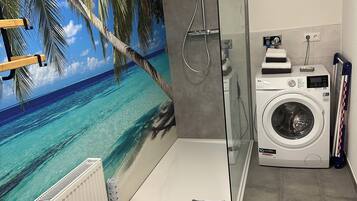 A bathroom with a glass-enclosed shower, a washing machine, and a mural of a beach scene.