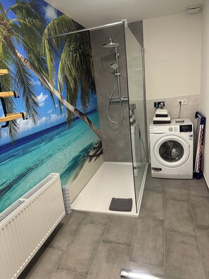 Een badkamer met een douchecabine van glas, een wasmachine en een muurschildering van een strand.