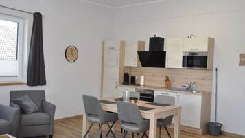 A compact living space with a kitchenette, a dining area with a table and chairs, a gray sofa, and a clock on the wall.