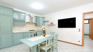 A kitchen with teal cabinetry, a marble countertop, a dining table with chairs, and a vase with flowers.