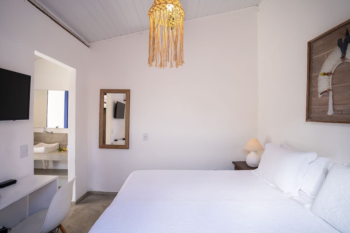 A hotel room with a large bed, a desk, a TV, a mirror, and a hanging light fixture.