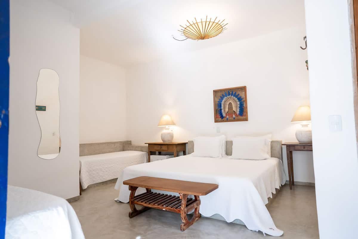 A bedroom with a bed, two bedside tables with lamps, a bench, a wall-mounted mirror, and a decorative headpiece.