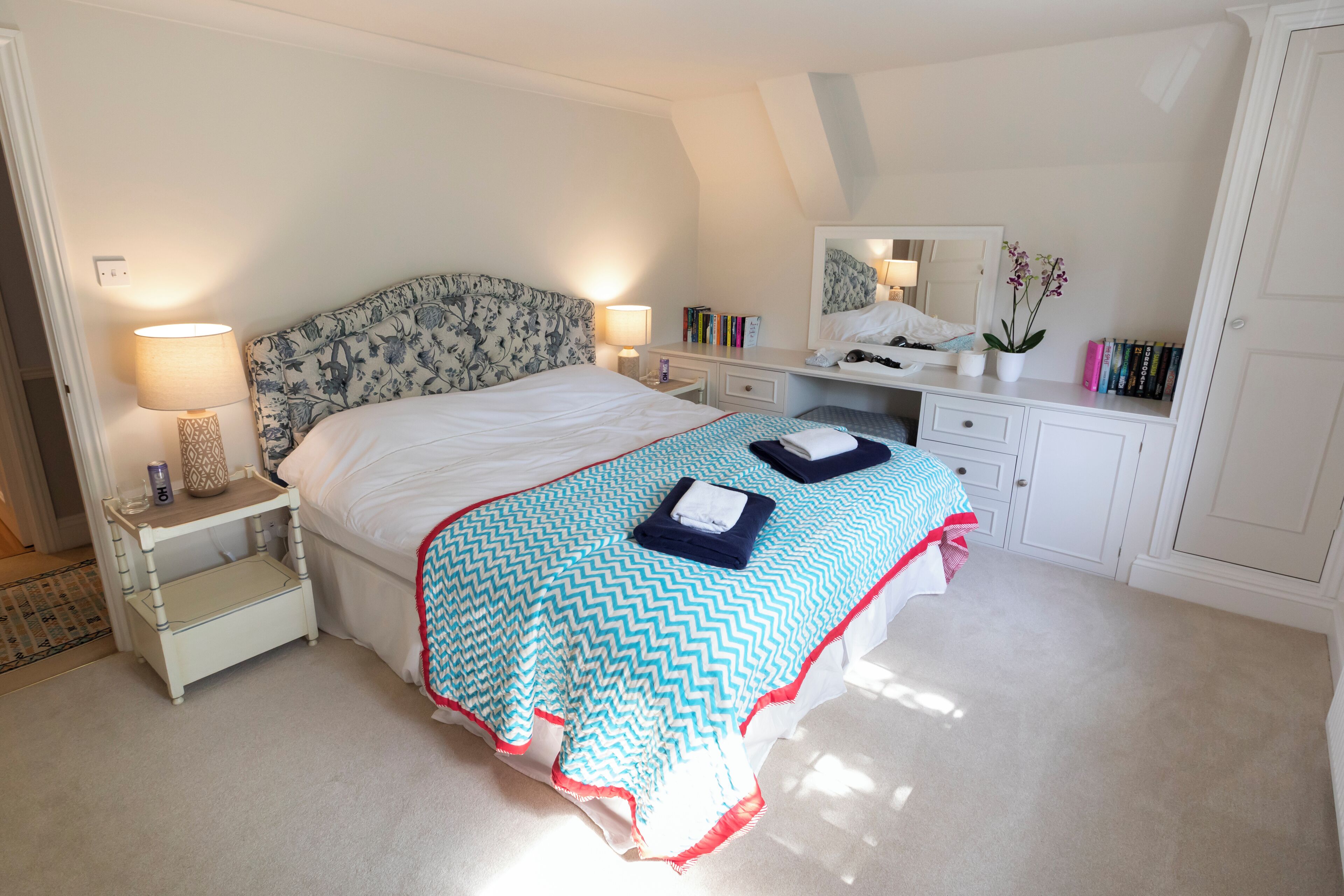 A bedroom with a bed, bedside tables, a desk, a mirror, and a bookshelf.