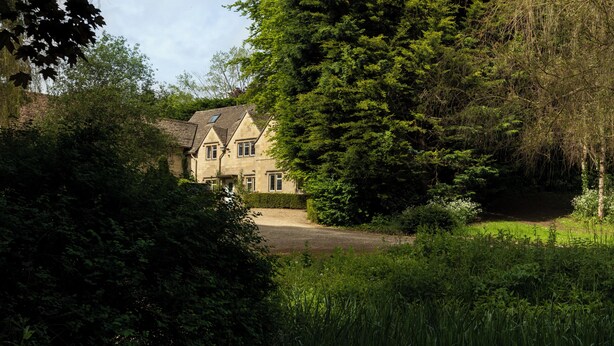 A large, two-story house with a prominent chimney, surrounded by dense greenery and trees.