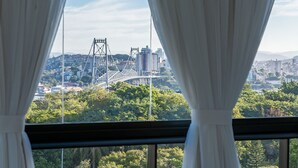 Blick durch ein Fenster mit Vorhängen auf eine Stadtansicht mit Gebäuden, einer Brücke und Grünflächen.