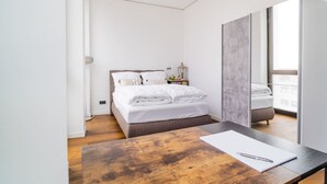 A modern bedroom with a large bed, a wooden desk, and a view of the outdoors.