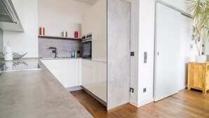 A modern kitchen with white cabinets, a grey countertop, and a wooden floor.