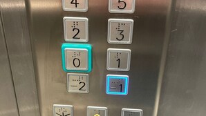 An elevator control panel with floor buttons numbered 0 to 5, a call button, a door open button, and a keypad with a lock symbol.