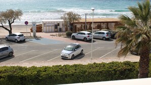 A parking lot with several cars, a beach, and a view of the ocean.