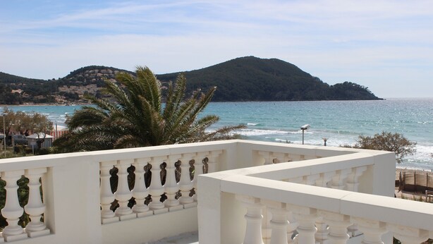 A balcony with white balustrades overlooking a coastal area with a mountain in the background.