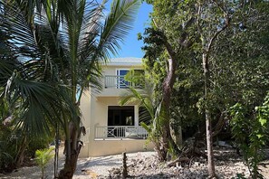 A two-story building with a balcony, surrounded by tropical vegetation.