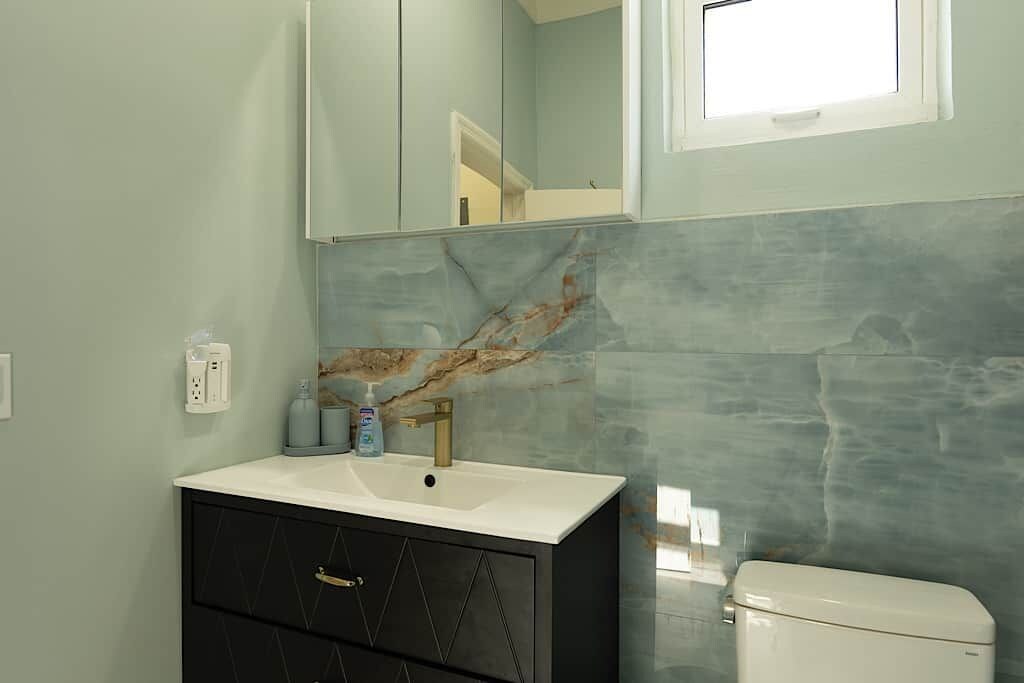 A bathroom with a white sink, a black cabinet with drawers, a marble backsplash, and a white toilet.