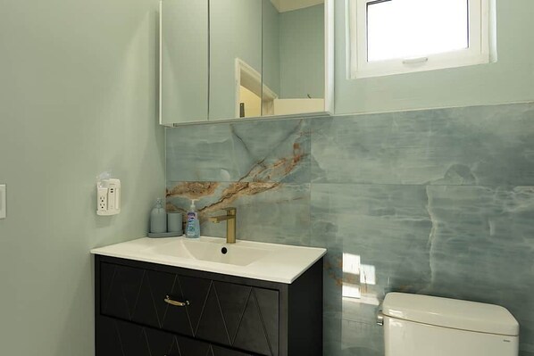 Une salle de bain avec un lavabo blanc, un meuble noir avec des tiroirs, un pare-feu en marbre et des toilettes blanches.