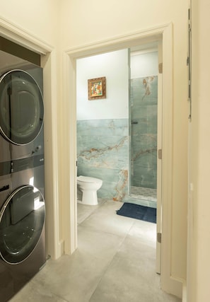 A hallway leading to a bathroom with a marble wall, a toilet, and a shower.