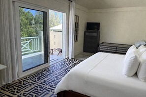 A hotel room with a bed, a television, a dresser, and a balcony with a view of trees.