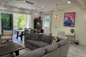 Un salon avec un canapé, une table à manger et des chaises, un ventilateur de plafond et un tableau accroché au mur.