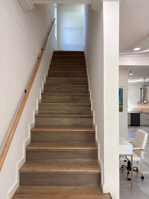 Eine Holztreppe mit Handlauf, die zu einem hellen Raum führt, wobei im Hintergrund eine Küchenzeile erkennbar ist.