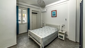 Un dormitorio con cama, mesitas de noche, una ventana con cortinas, aire acondicionado y un cuadro en la pared.