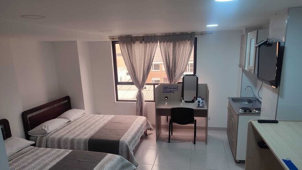A hotel room with two beds, a desk, a chair, a TV, and a kitchenette. - Hotel torre 15  (Bogotá)