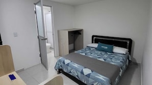 A bedroom with a bed, a desk, and a bathroom visible through an open door. - Hotel torre 15  (Bogotá)