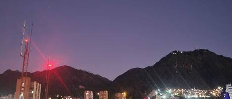 A cityscape at dusk with buildings and a mountain in the background.