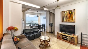 A modern living room with a sofa, a coffee table, a TV, and a dining area with chairs and a table. - Les Pénates - Meublé 3 étoiles - Vue mer (Arrondissement of Saint-Pierre)
