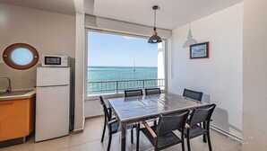 A compact kitchen with a microwave, a sink, and a dining area with a table and chairs. A large window offers a view of the sea. - Les Pénates - Meublé 3 étoiles - Vue mer (Arrondissement of Saint-Pierre)