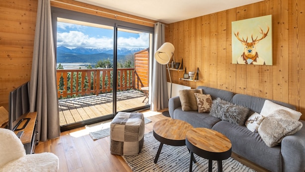 A cozy living room with a grey sofa, wooden coffee table, and a view of mountains through a sliding glass door.