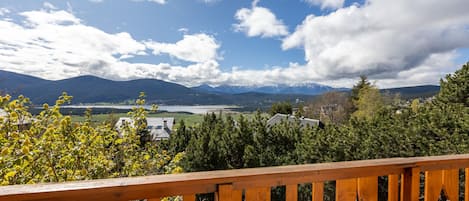 Um deck de madeira com vista para montanhas, um lago e uma cidade ao longe.