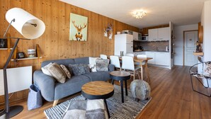 A modern living room with a grey sofa, round wooden tables, and a kitchen in the background.