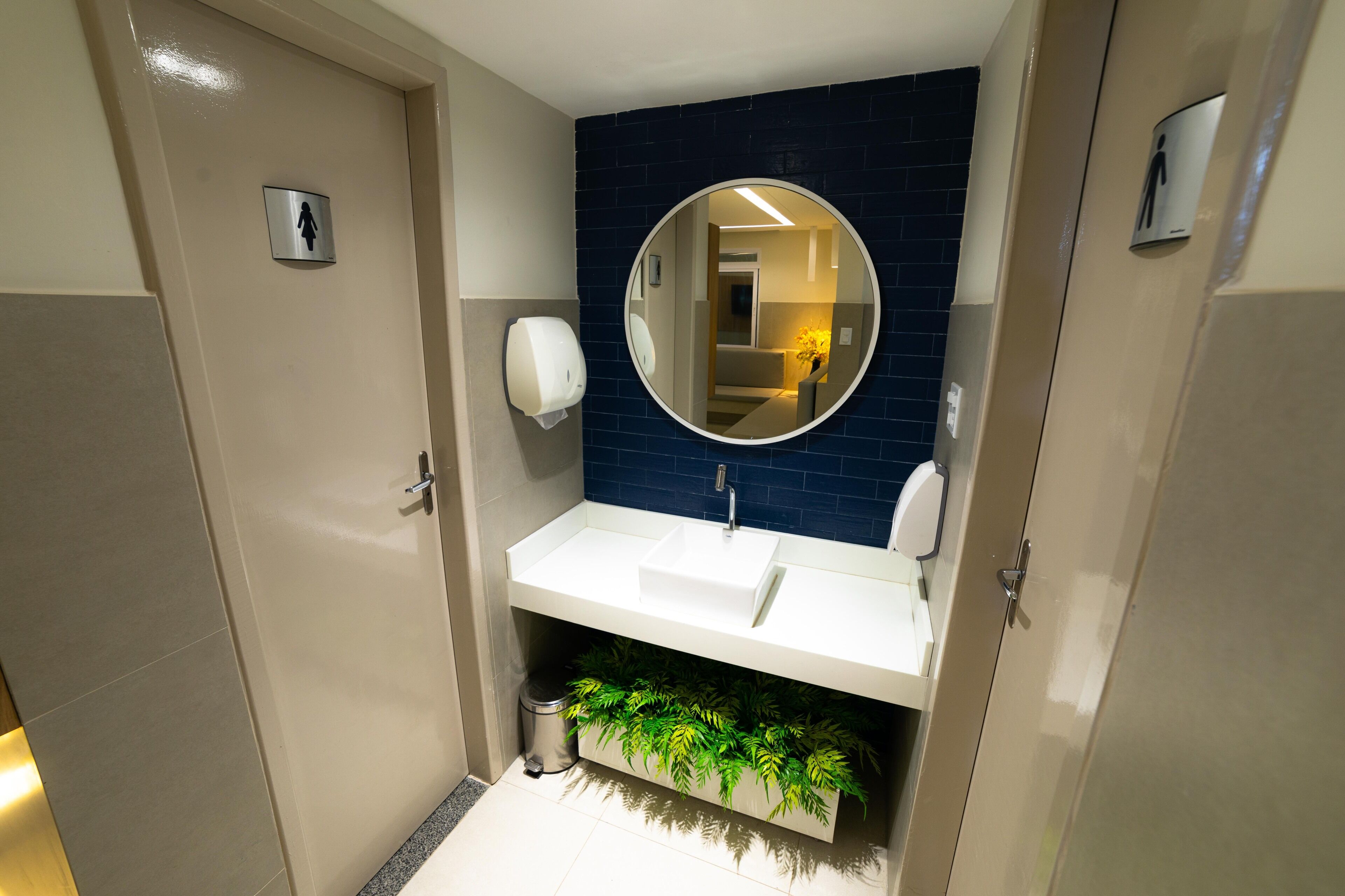 A modern bathroom with a white sink, a mirror, and a trash bin.