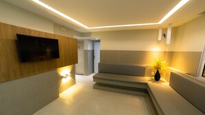A modern interior with a flat-screen TV mounted on a wooden panel, a seating area with a vase of flowers, and a staircase leading to another room. - Hotel Pousada do Farol (Aracaju)