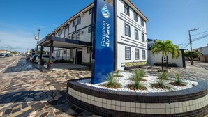 A building with a sign reading "Pousada do Faro". It features a tiled facade, a covered entrance, and a landscaped area with plants and a circular stone border. - Hotel Pousada do Farol (Aracaju)