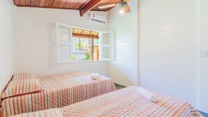 A bedroom with two beds, wooden ceiling, white walls, and a window with an open shutter. - GB69 Excelente Casa a 400m da Praia (Camaçari)