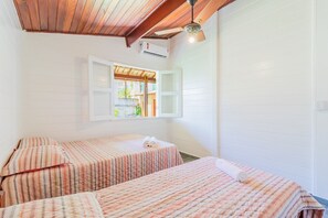 Une chambre avec deux lits, un plafond en bois, des murs blancs et une fenêtre dont le volet est ouvert.