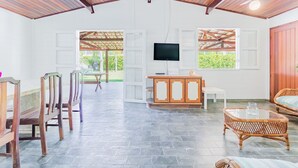 A spacious room with a high ceiling, a television mounted on the wall, a dining area with wooden chairs, a wicker sofa, and a stone-tiled floor. - GB69 Excelente Casa a 400m da Praia (Camaçari)