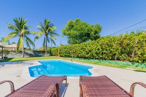 A swimming pool with lounge chairs, surrounded by palm trees and a hedge. - GB69 Excelente Casa a 400m da Praia (Camaçari)