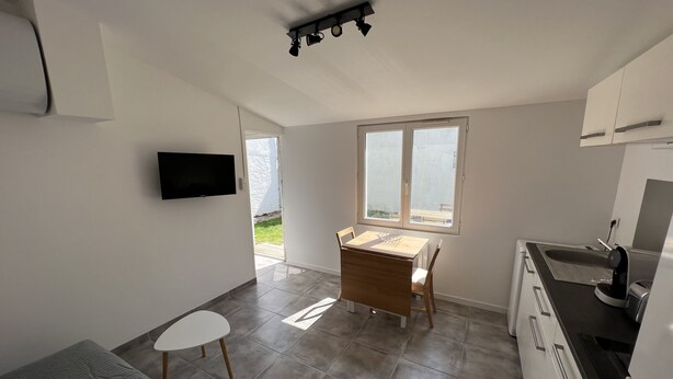 A modern kitchen with a built-in oven, a dining area with a table and chairs, and a large window offering a view of the outdoors. - Petite Maison au Calme Dans un Village Typique (Saint-Pierre-d'Oléron)