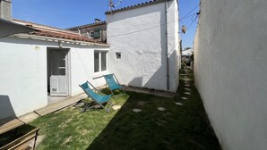 A small, white-walled building with a tiled roof, a wooden bench, and two green lawn chairs in the yard. - Petite Maison au Calme Dans un Village Typique (Saint-Pierre-d'Oléron)