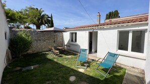 A small house with a stone wall, a patio with a table and chairs, and a covered area with two chairs. - Petite Maison au Calme Dans un Village Typique (Saint-Pierre-d'Oléron)