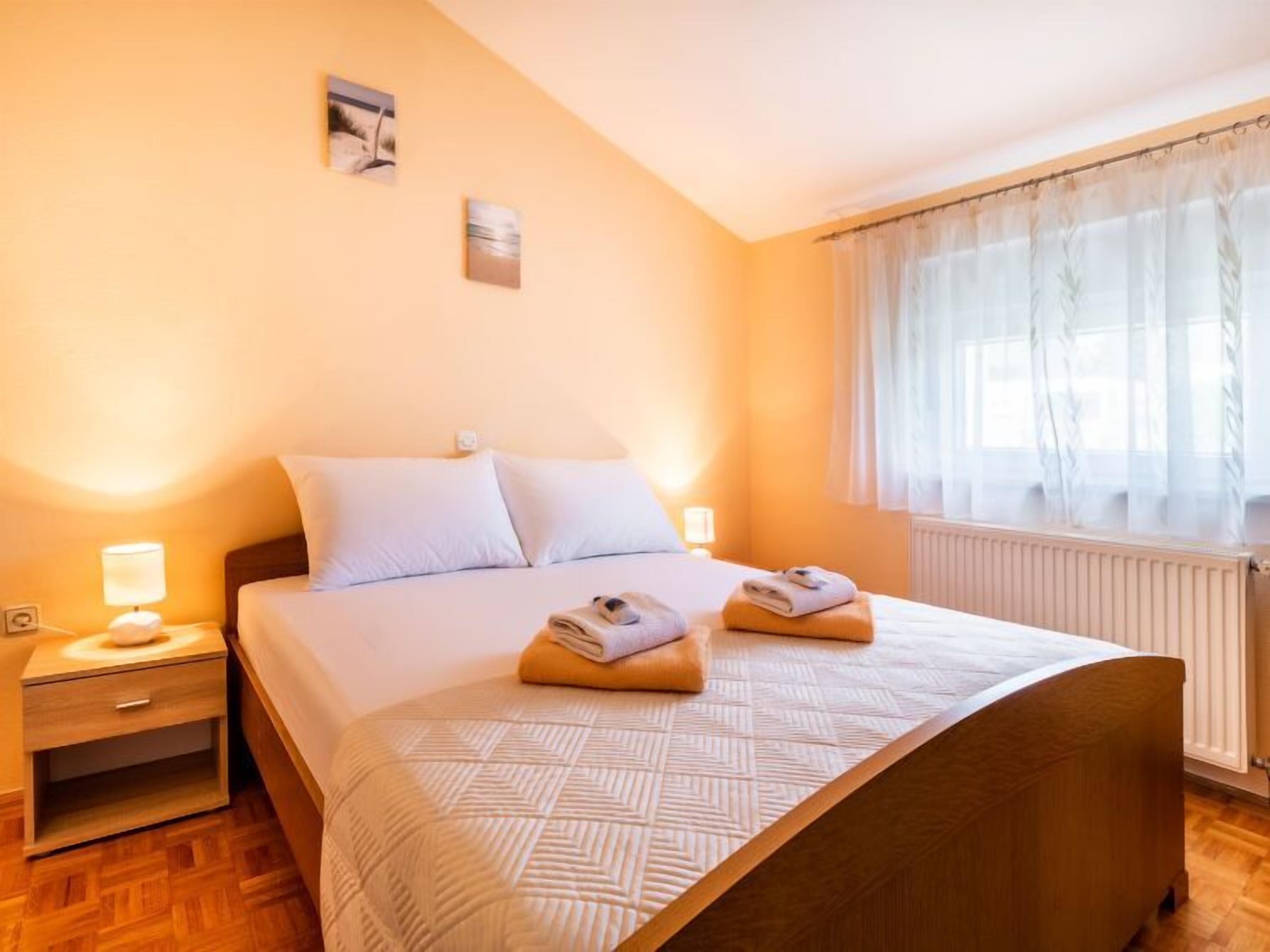 Une chambre d’hôtel avec un lit, une table de chevet, une lampe et une fenêtre avec des rideaux légers.