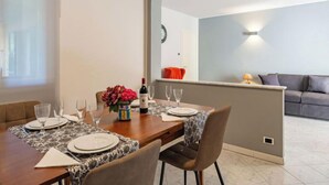 A dining area with a wooden table set for four, a vase of flowers, and a bottle of wine. - Stazione by Interhome (Porlezza)