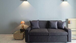A modern living room with a dark grey sofa, two wall-mounted lamps, a small side table with a lamp, and a radiator. - Stazione by Interhome (Porlezza)